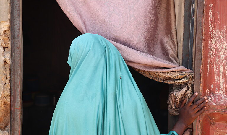 Ein Mädchen mit Kopftuch von hinten steht in einem Türrahmen