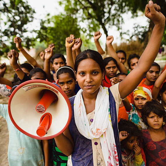 Mädchen und Frauen aus Indien bei einer Demonstration mit Megafon Eine Gruppe von Mädchen und Frauen aus Indien hebt die Fäuste und demonstriert, während eines der Mädchen ein Megafon hält.
