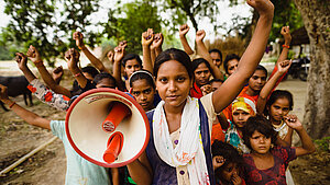 Eine Gruppe von Mädchen und Frauen aus Indien hebt die Fäuste und demonstriert, während eines der Mädchen ein Megafon hält.