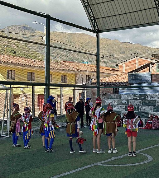 Kinder sammeln sich auf einem Sportplatz unter einer Überdachung.