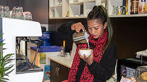Junge Frau in Nepal bereitet in einer Café-Ausbildung professionell einen Cappuccino zu