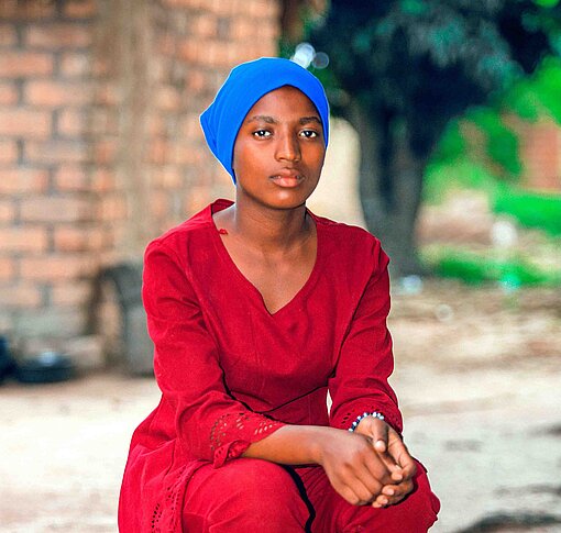 Eine junge Frau in rotem Kleid sitzt auf einer Bank und schaut ernst