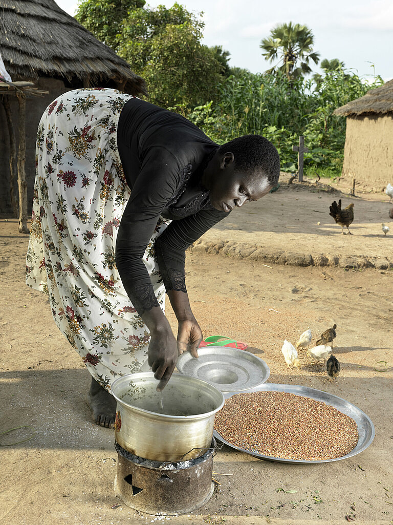 Eine Frau steht vor einem Topf, der auf dem Boden steht, beugt sich vor und bereitet essen zu