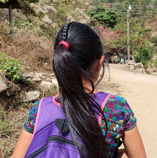 Ein Mädchen mit Schulranzen auf einer Feldstraße