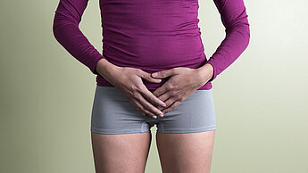 Der Torso einer Frau, sie hält die Hände über ihren Bauch