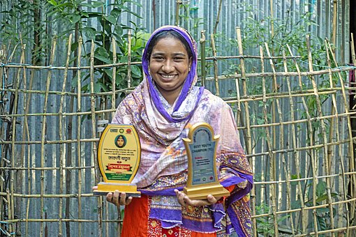 Ein Mädchen in bunter Kleidung zeigt zwei golden glänzende Trophäen