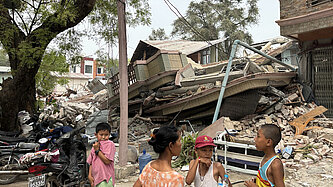 Eine Gruppe von Kindern steht vor den Ruinen eines zerstörten Hauses.
